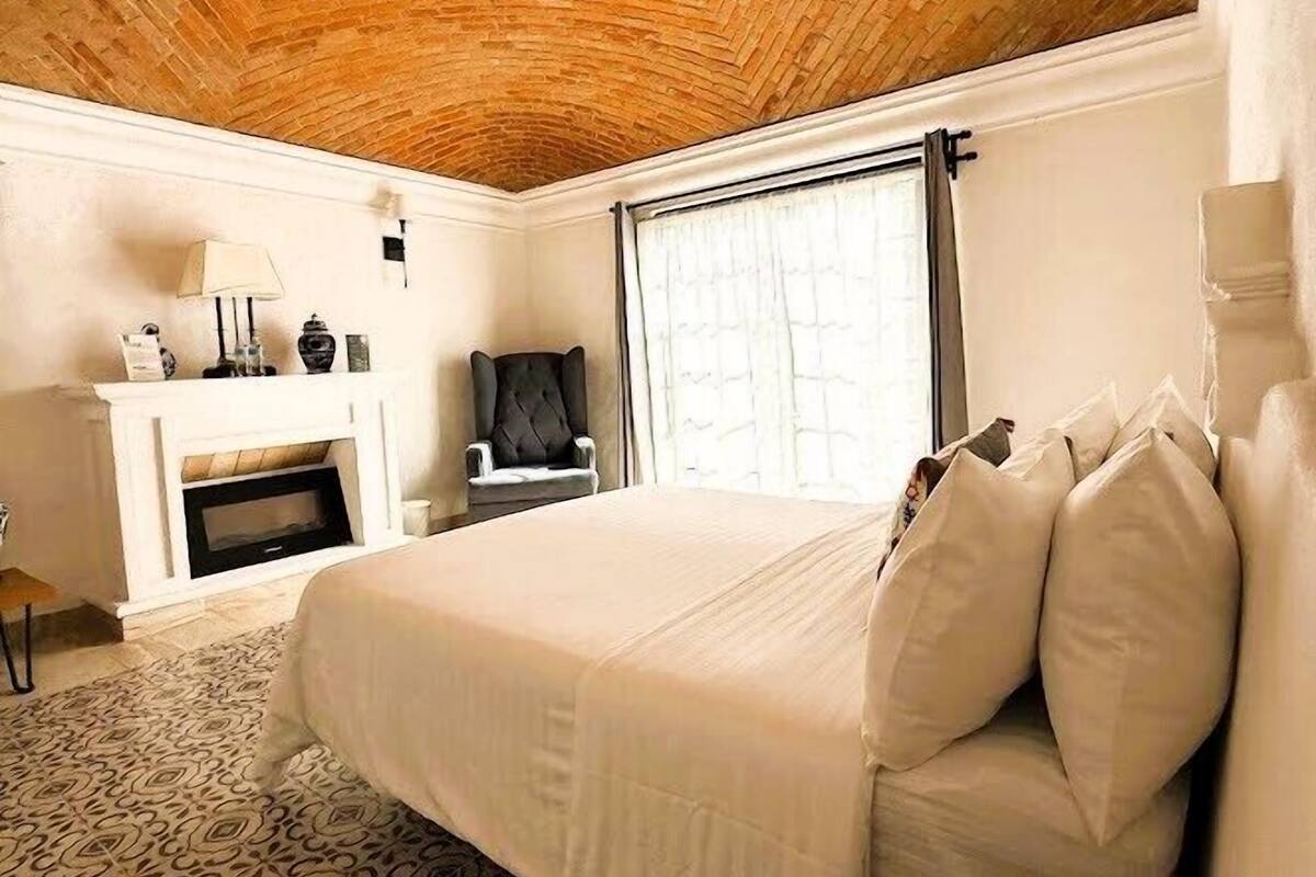 A bedroom with a brick ceiling, a bed with white bedding, a patterned rug, and a small table.