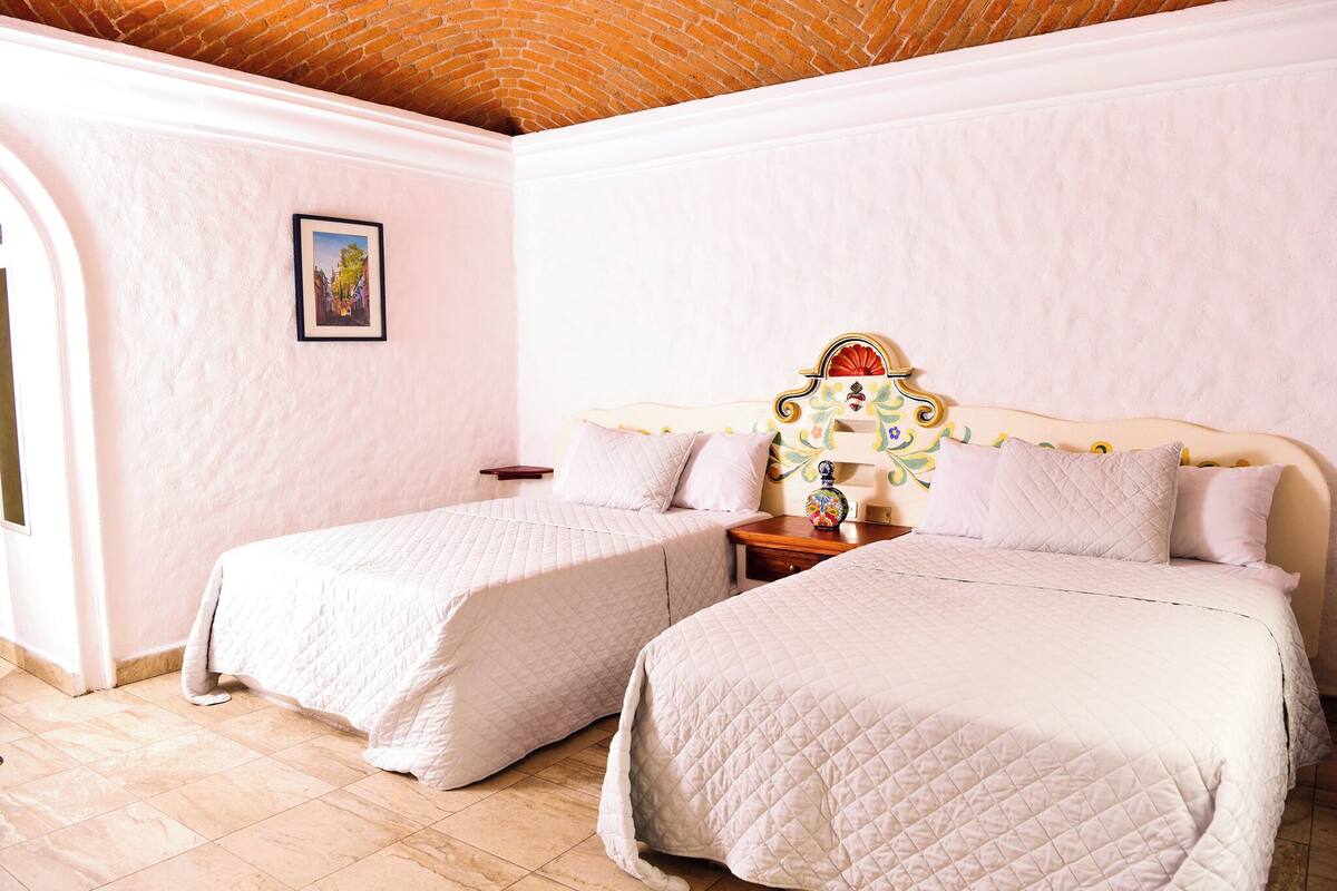 A hotel room with two beds, a wooden headboard, a small bedside table, and a picture on the wall.