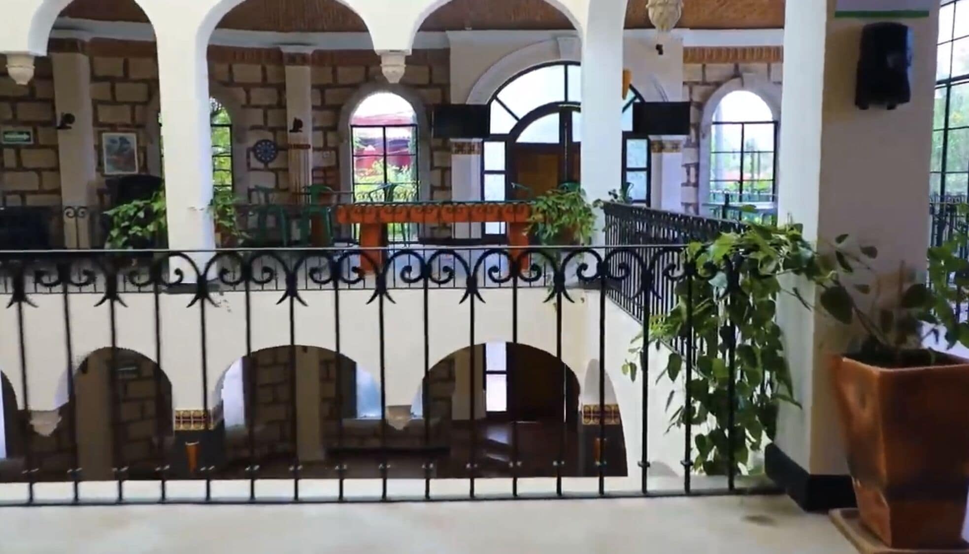 A courtyard with a wrought iron fence, potted plants, and arched windows.
