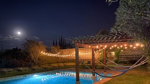 A swimming pool with a pergola and string lights, surrounded by a brick wall and greenery.