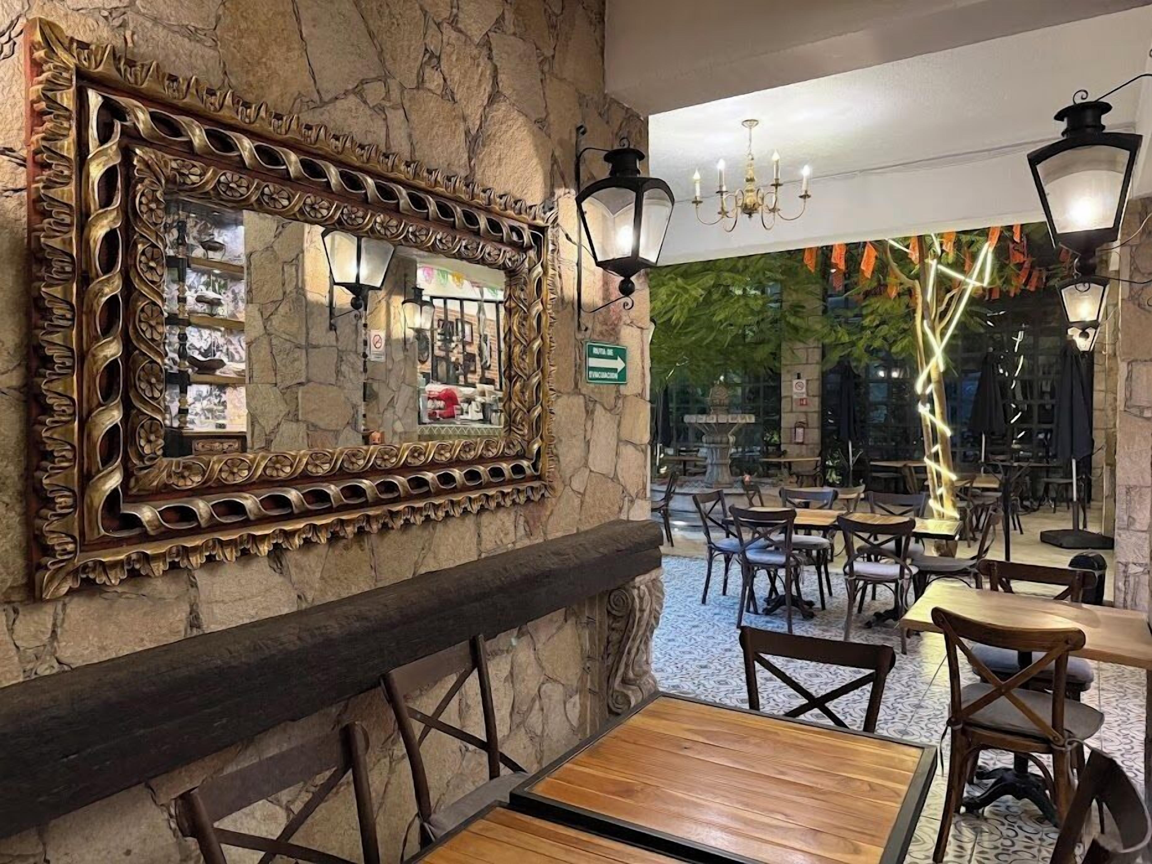 A restaurant interior with stone walls, a large ornate mirror, wooden tables and chairs, and hanging lanterns.