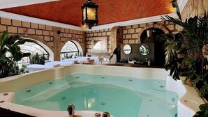 A spa area with a large hot tub, stone walls, and arched windows.