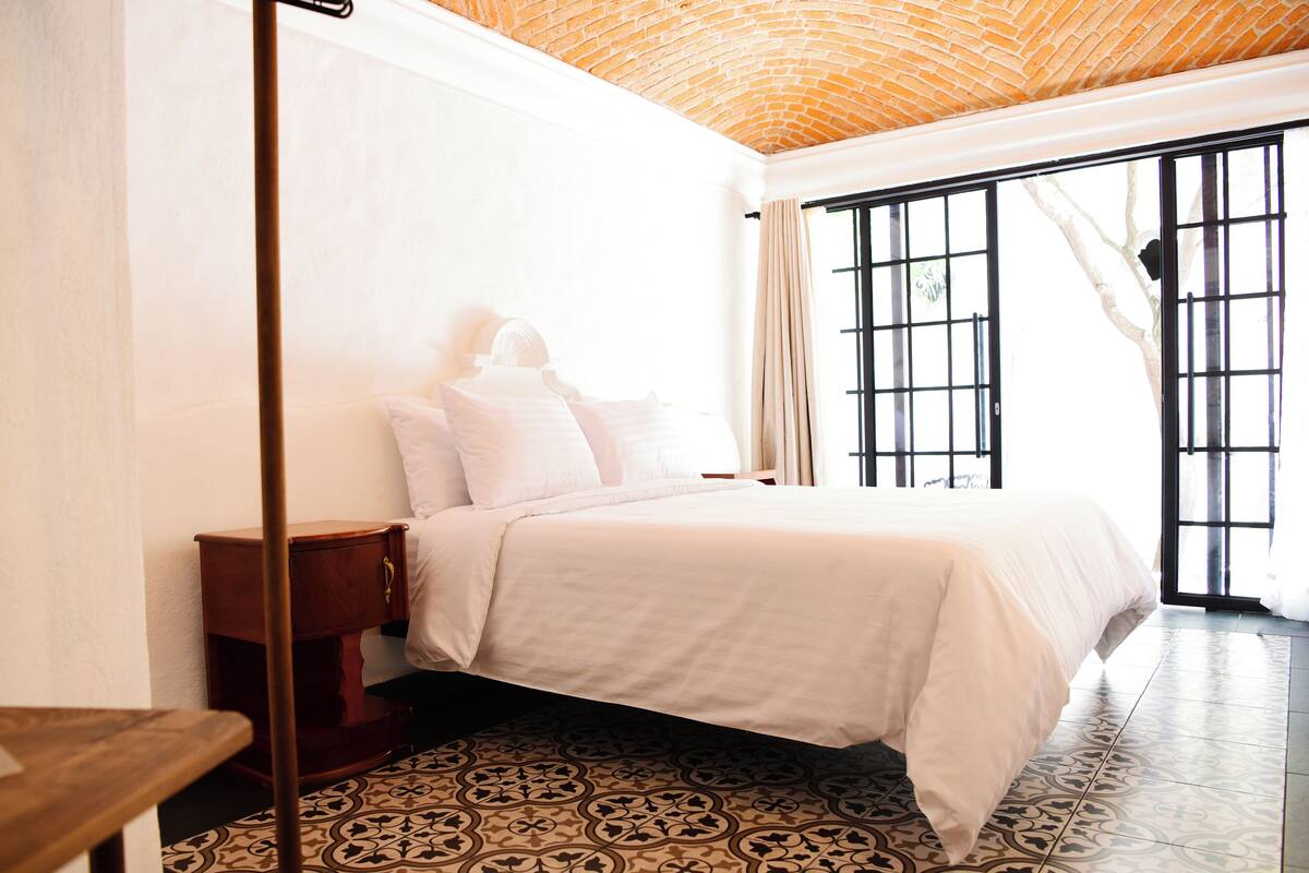 A bedroom with a bed, a nightstand, a patterned floor, and a brick ceiling.