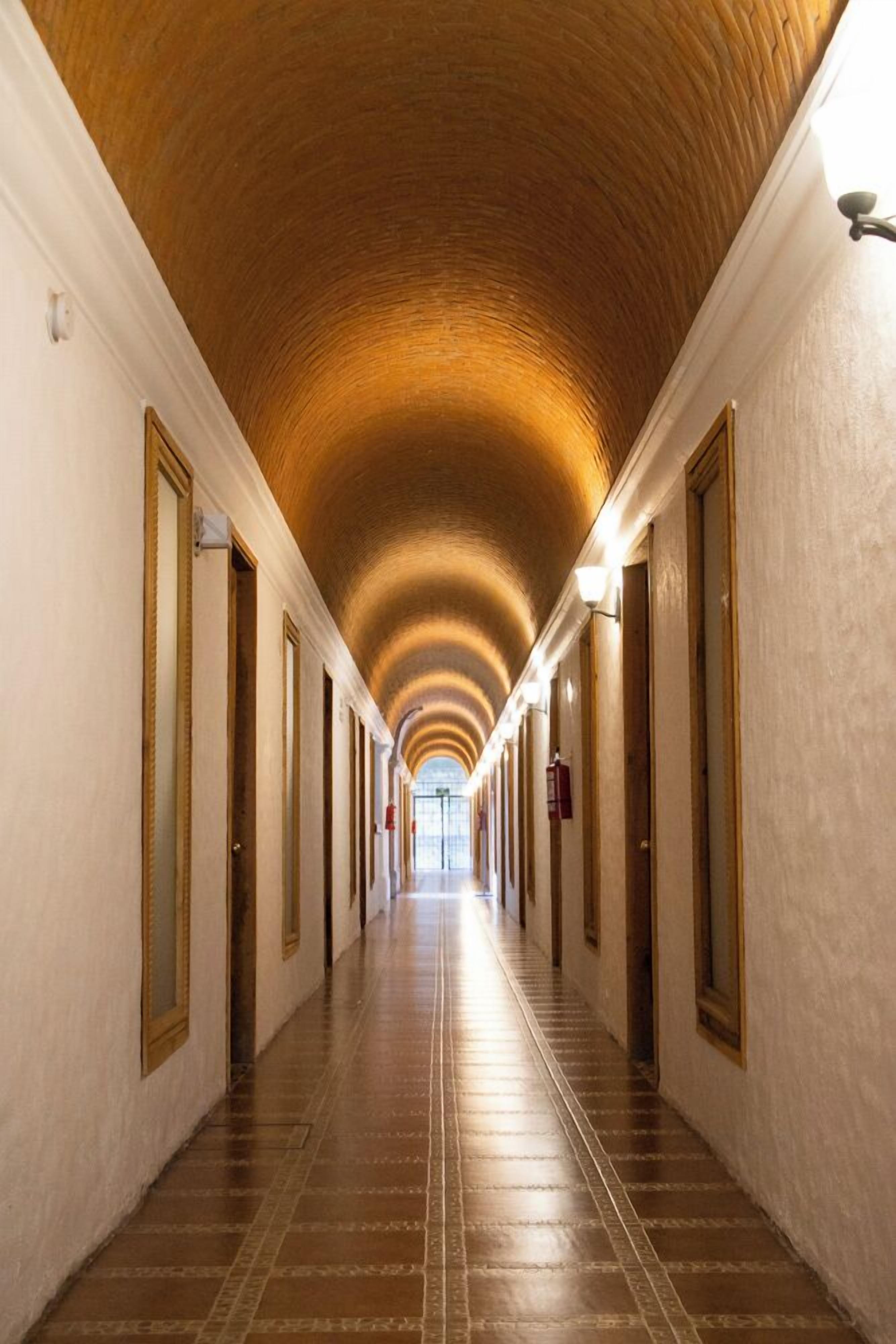 A long, narrow hallway with a vaulted ceiling and a series of doors on one side.