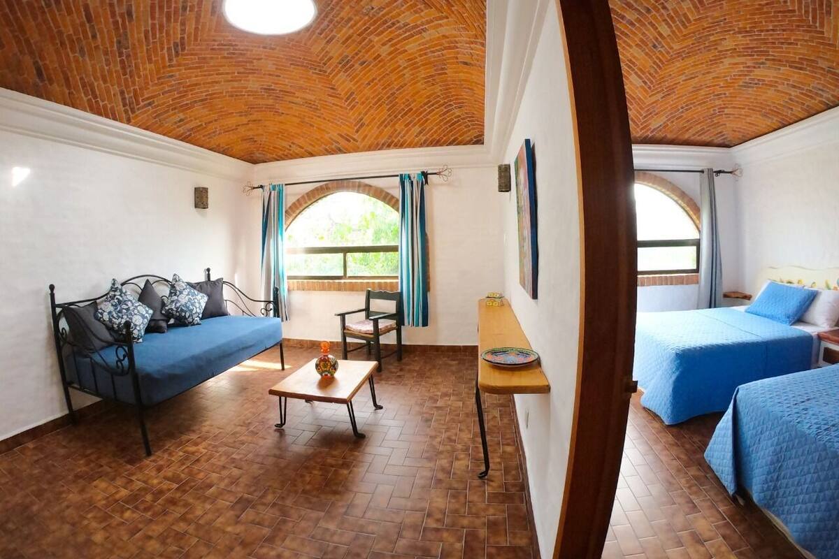 A room with a brick ceiling, a sofa, a bed, a table, and a window with curtains.