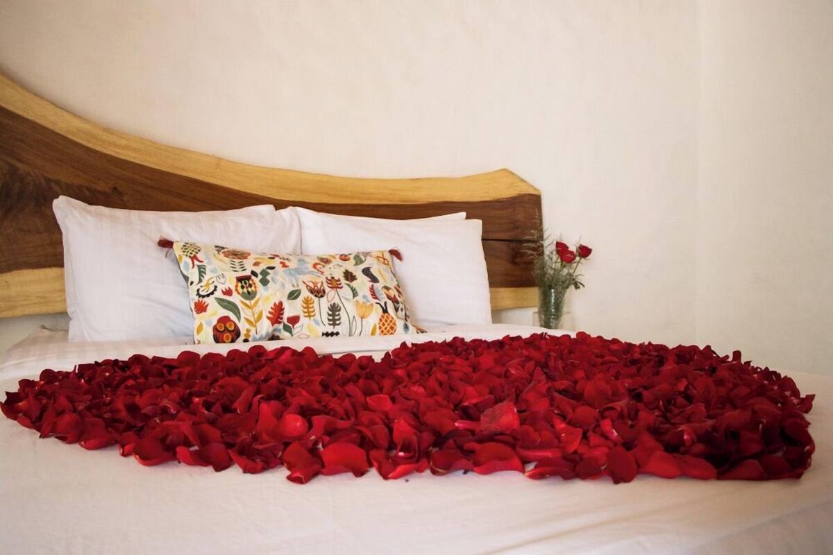 A bed with a white sheet, a floral pillow, and a bedspread covered in red rose petals.