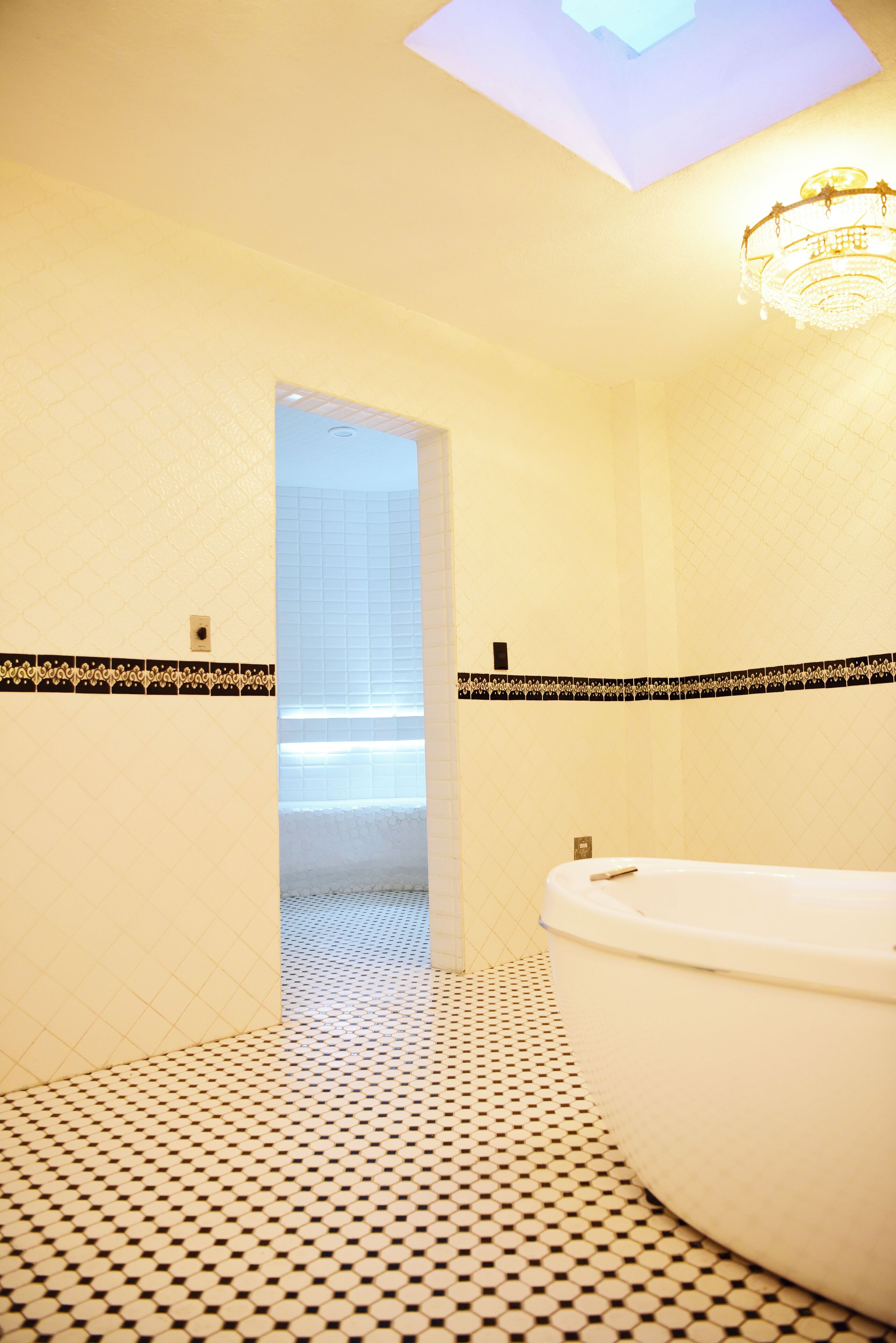 Un baño con una bañera blanca, piso con estampado blanco y negro, y un tragaluz sobre la zona de la ducha.