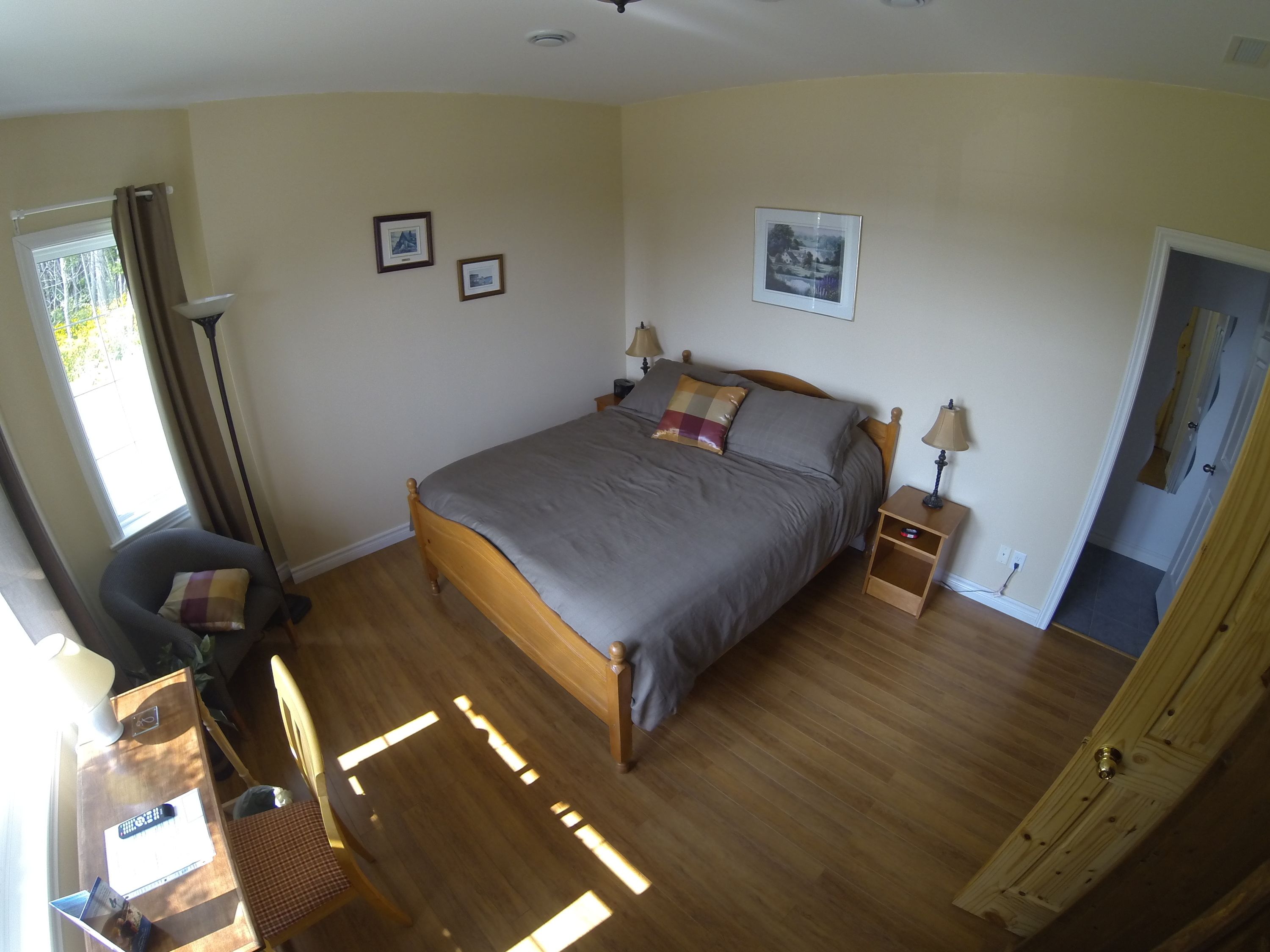 A bedroom with a wooden bed, two bedside tables with lamps, a desk with a chair, and a window with curtains.
