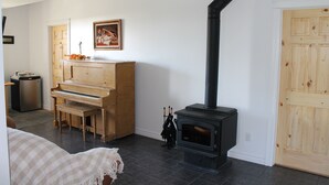 Una habitación con un piano, un estufa de leña negra y una puerta de madera.