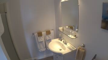 A bathroom with a sink, mirror, and toilet. There are towels hanging on the wall and a shower area.