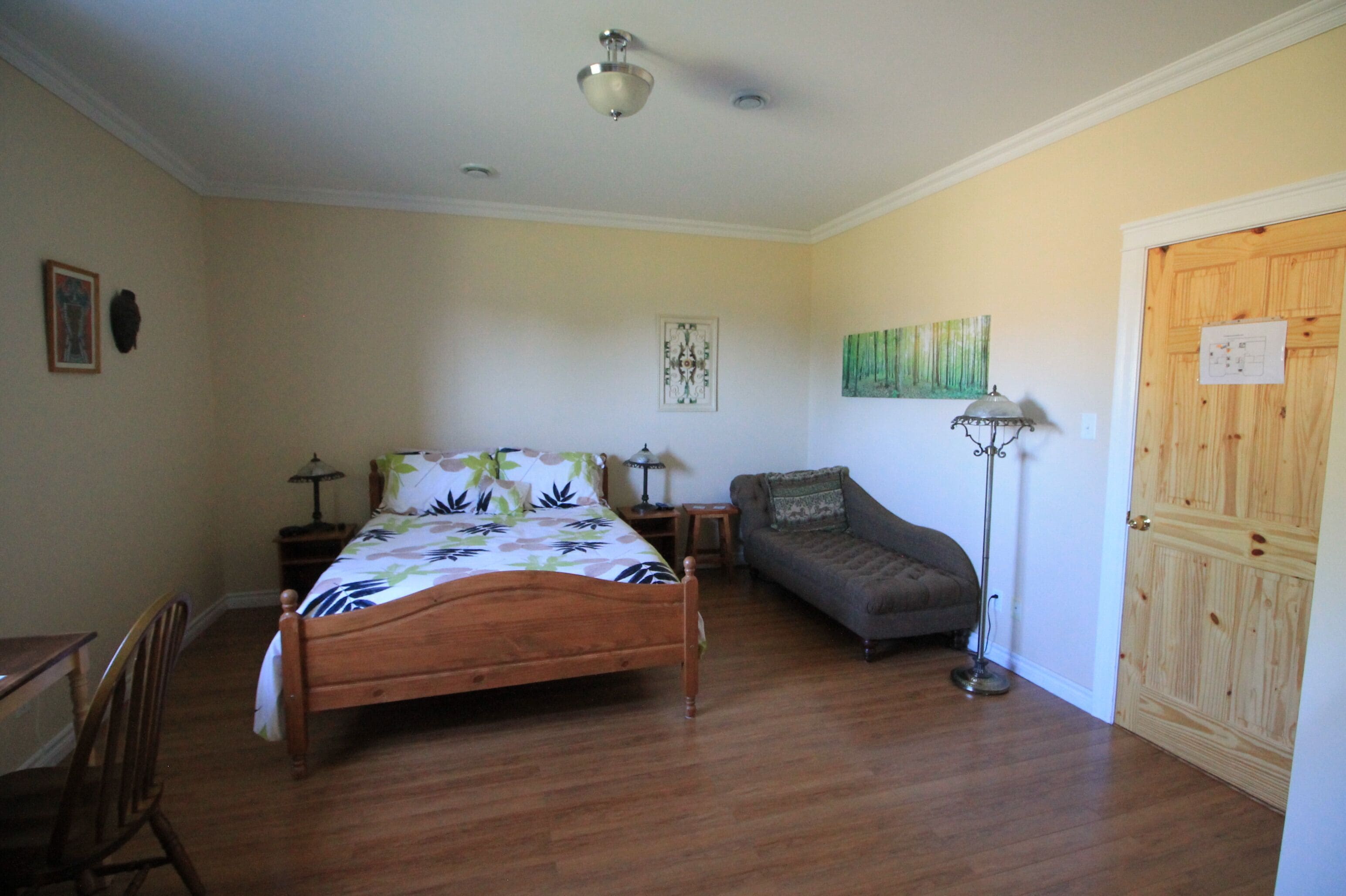 A bedroom with a wooden bed, a nightstand, a floor lamp, a sofa, and a wooden door.