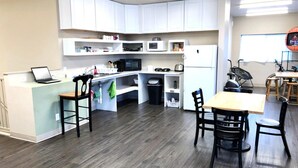 A compact kitchen with white cabinets, a microwave, a refrigerator, a sink, and a dining area with a table and chairs. - SLC Hostel (Salt Lake City)