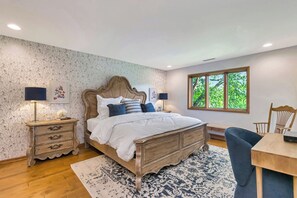 A bedroom with a wooden bed, two bedside tables, a desk, and a window with a view of trees.