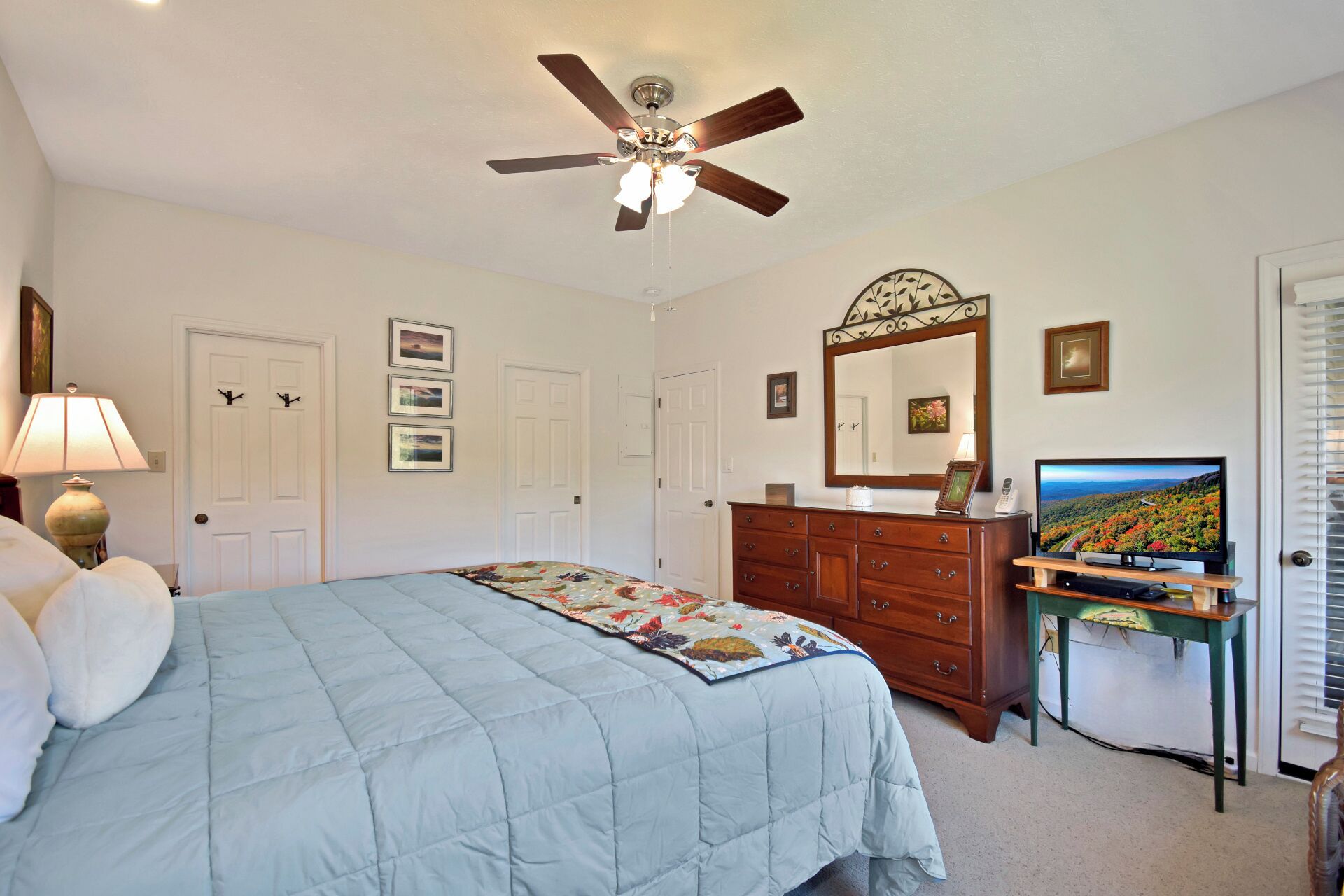 A bedroom with a bed, a dresser, a TV, a ceiling fan, and a door.