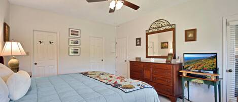 A bedroom with a bed, a dresser, a TV, a ceiling fan, and a door.