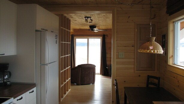 A wooden interior with a kitchen area, a dining table, and a view through a door. - Cape Split View Cottages (West Bay)