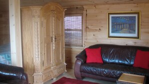 A wooden-paneled room with a leather sofa, a wooden cabinet, and a framed picture on the wall. - Cape Split View Cottages (West Bay)