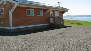 A wooden cabin with a gravel driveway, a wooden porch, and a view of the water. - Cape Split View Cottages (West Bay)