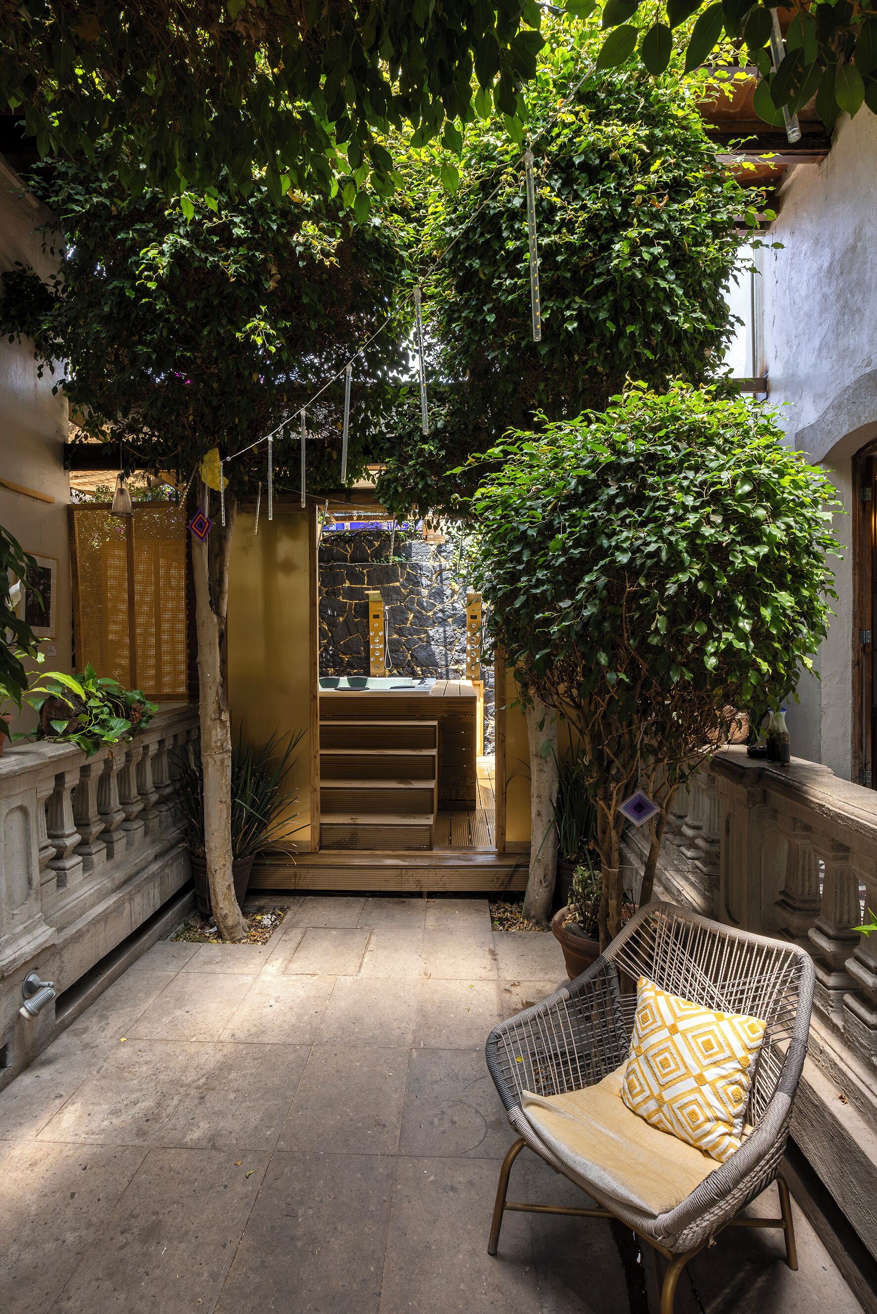 A courtyard with a wicker chair, a stone wall, and a small building with a stone facade.