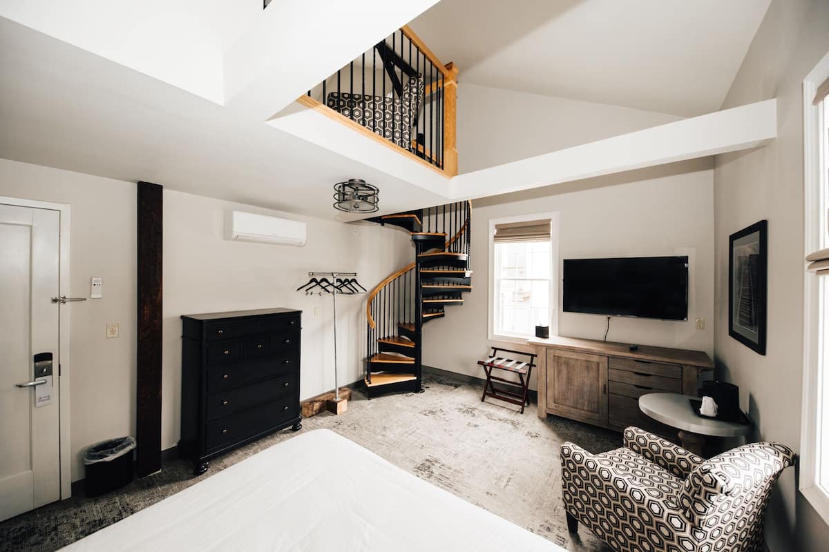 Un dormitorio con cama, cómoda, televisor, escalera y ventana.