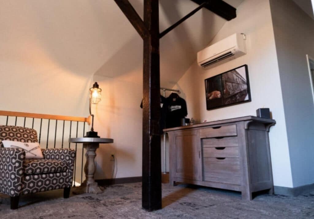 A room with a patterned sofa, a small round table, a cabinet, and a ceiling beam.