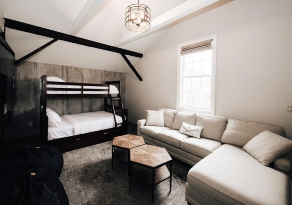 A bedroom with a bunk bed, a sofa, a coffee table, and a window with blinds.