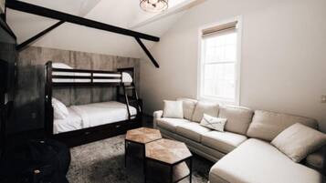 A bedroom with a bunk bed, a sofa, a coffee table, and a window with blinds.