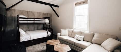 A bedroom with a bunk bed, a sofa, a coffee table, and a window with blinds.