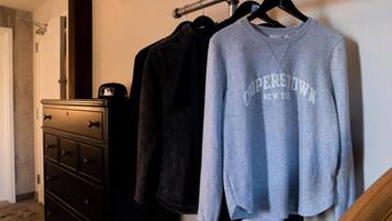 Una habitación con un aparador, un perchero con ropa y una sudadera gris con la leyenda 'COPENHAGEN NEW YORK'.