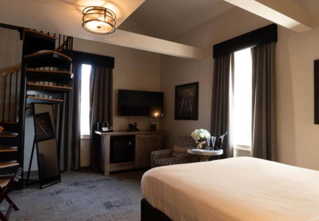 A hotel room with a bed, a desk, a chair, a television, and a staircase.