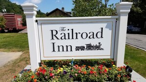 A sign for The Railroad Inn with a flower bed in front. - The Railroad Inn (Cooperstown)