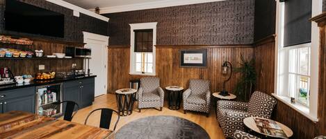 A cozy living room with a wooden paneled wall, a large window, and a dining area with a wooden table and chairs.