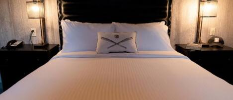 Una cama con cabecera, dos mesitas de noche con lámparas y un cojín con diseño.