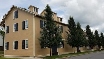 A two-story house with a beige exterior, multiple windows with shutters, and a well-maintained lawn.