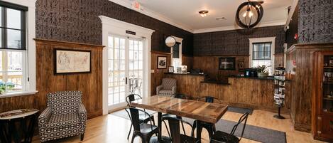 A dining area with a wooden table and chairs, a patterned armchair, and a large window with a view.