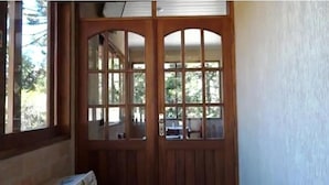 A wooden door with glass panels, a window to the left, and a view of a backyard with a car and a chair. - Hotel Vill' Agi (Campos do Jordão)