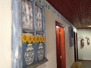 A hallway with a wooden ceiling, a door, and a wall with a floral pattern and sunflowers. - Hotel Vill' Agi (Campos do Jordão)