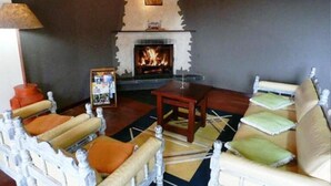 A cozy living room with a fireplace, a sofa, a chair, and a small table. - Hotel Vill' Agi (Campos do Jordão)