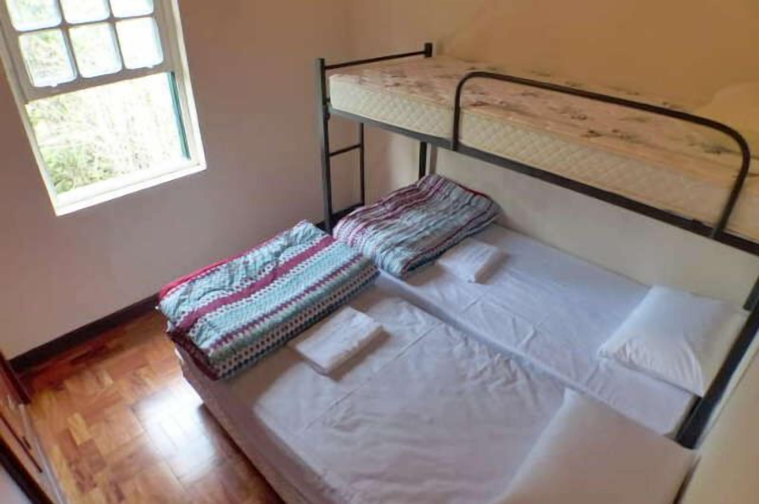 A bunk bed room with a window, wooden flooring, and a plain wall.
