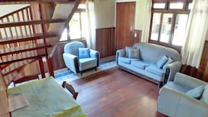 A living room with a wooden staircase, a sofa, two armchairs, and a table covered with a yellow cloth.
