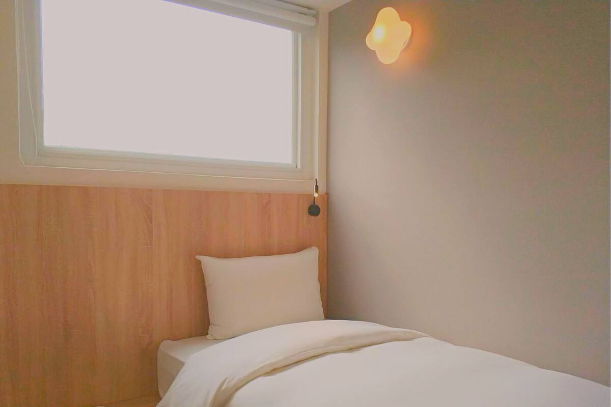 Ein Schlafzimmer mit hölzernem Kopfteil, einem weißen Bett und einem Fenster mit Leuchte.