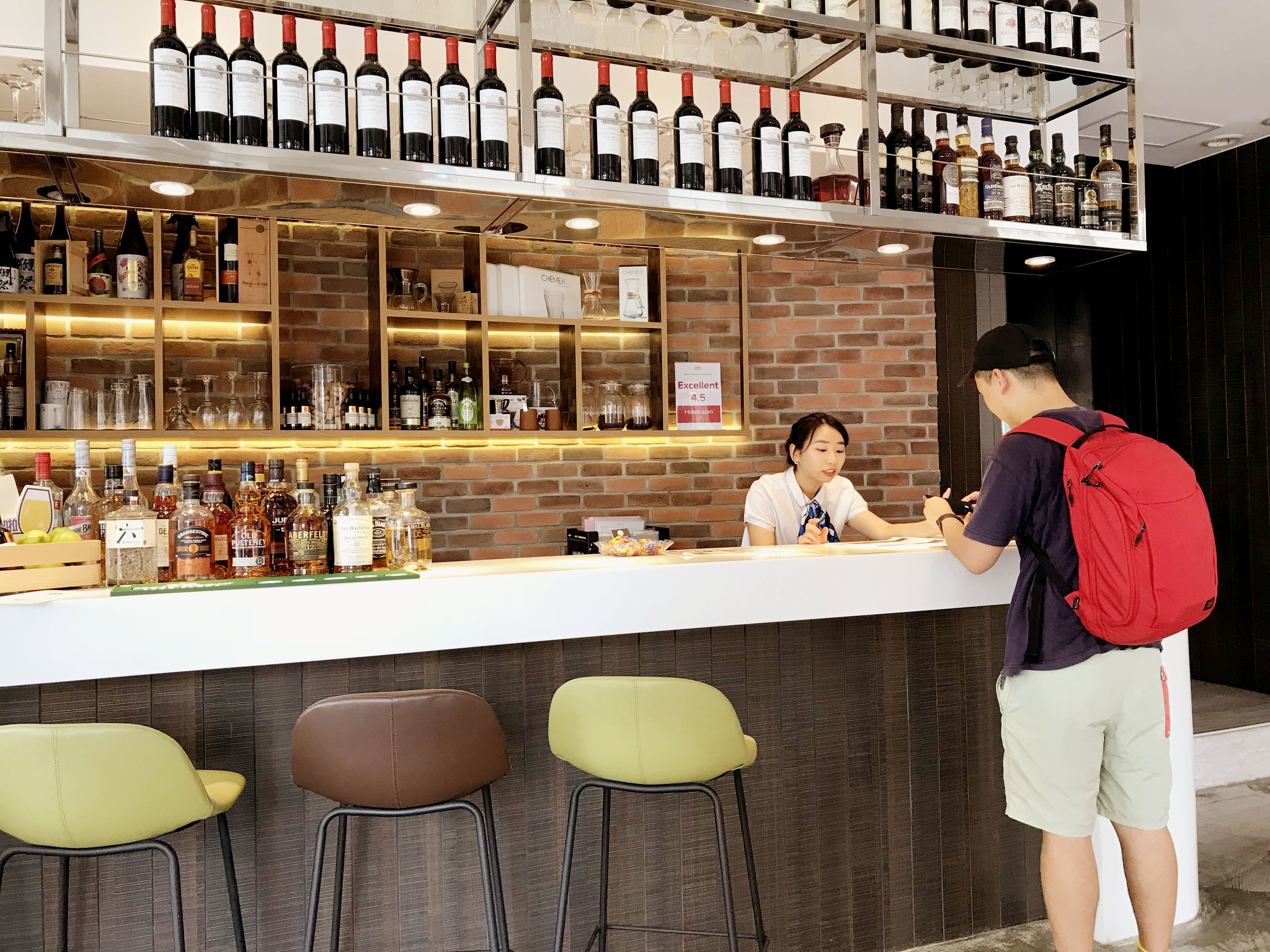 A bar area with a variety of liquor bottles and glasses on shelves. There are stools and a counter where a person is standing.