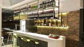 A modern bar area with a long counter, multiple shelves of wine bottles, and a brick wall backdrop. - Single Inn Kaohsiung Station Hostel (Kaohsiung)