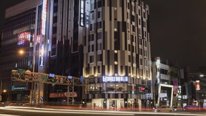 A modern hotel with a prominent sign, multiple floors, and a busy street with traffic lights and signage. - Single Inn Kaohsiung Station Hostel (Kaohsiung)