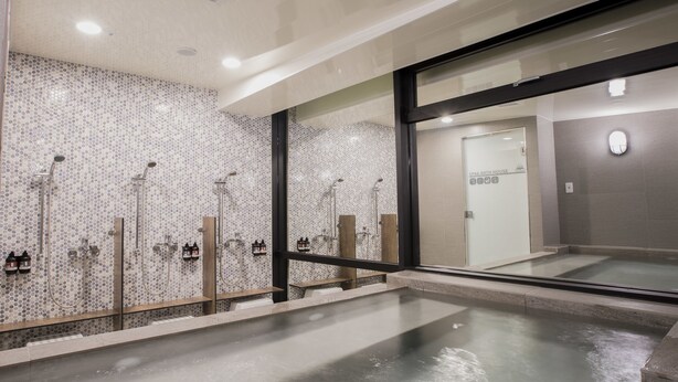 A modern bathroom with multiple showerheads, a large mirror, and a glass door leading to another room. - Single Inn Kaohsiung Station Hostel (Kaohsiung)