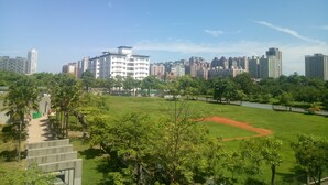 A park with a baseball field, surrounded by trees and a city skyline in the background. - Tainan Here Hostel (Tainan)