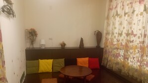 A cozy living room with a round wooden table surrounded by colorful cushions, a sofa with patterned cushions, a decorative vase, and a wall-mounted lamp. - Tainan Here Hostel (Tainan)