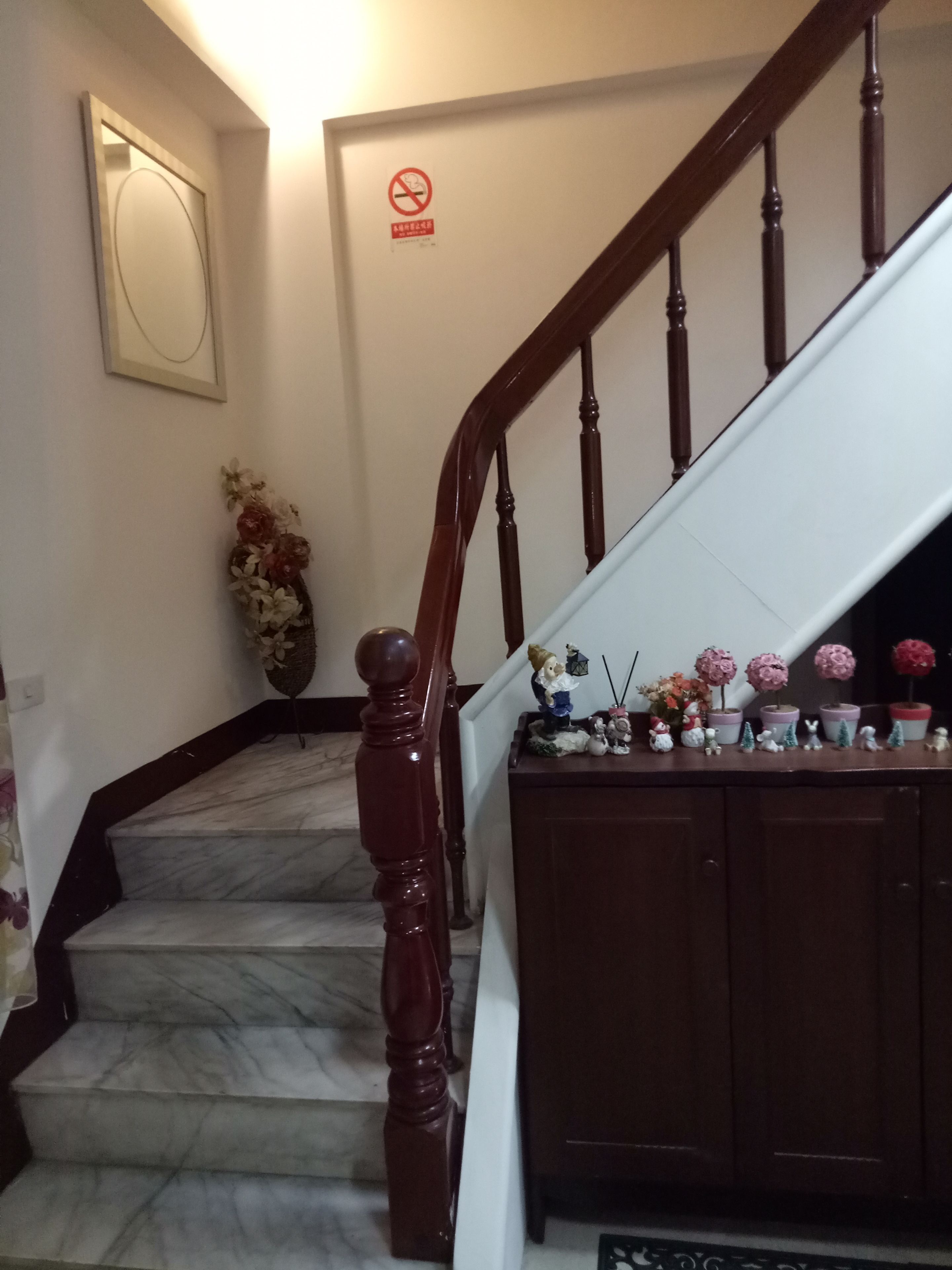 A staircase with a wooden handrail and marble steps, leading to a landing with a white wall and a 'no smoking' sign.