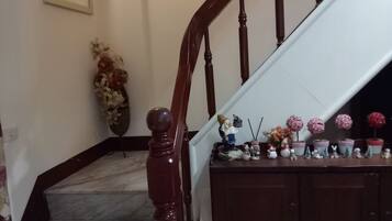 Una escalera con barandilla de madera y peldaños de mármol, que conduce a un rellano con pared blanca y un cartel de 'no fumar'.