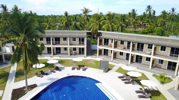 A modern hotel with a swimming pool, lounge chairs, and palm trees. - Malinawon Resort (Panglao)